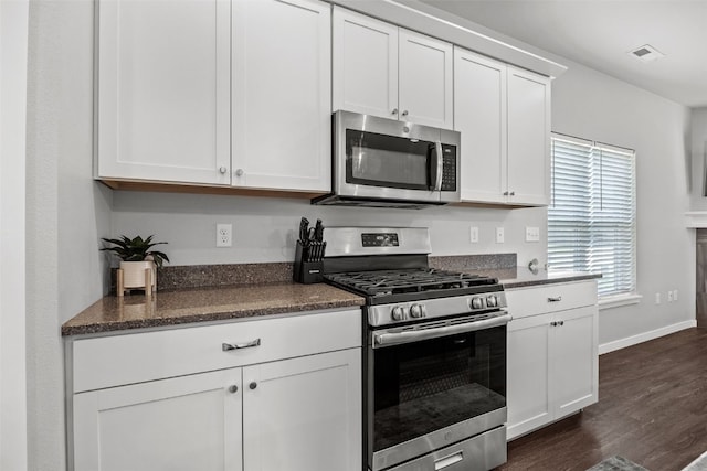 kitchen featuring stainless steel appliances, dark wood finished floors, white cabinetry, dark stone counters, and baseboards