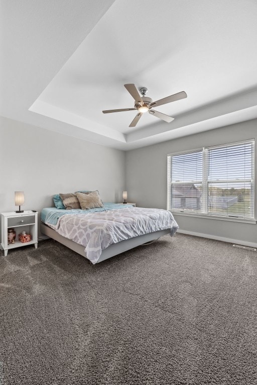carpeted bedroom featuring a raised ceiling, a ceiling fan, and baseboards