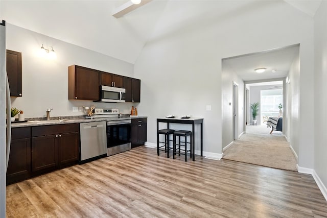 kitchen with appliances with stainless steel finishes, dark brown cabinetry, light wood-style flooring, a sink, and baseboards