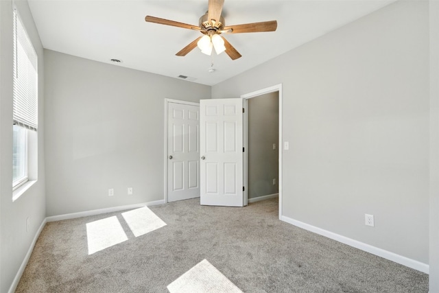 unfurnished bedroom featuring light carpet, multiple windows, baseboards, and a ceiling fan