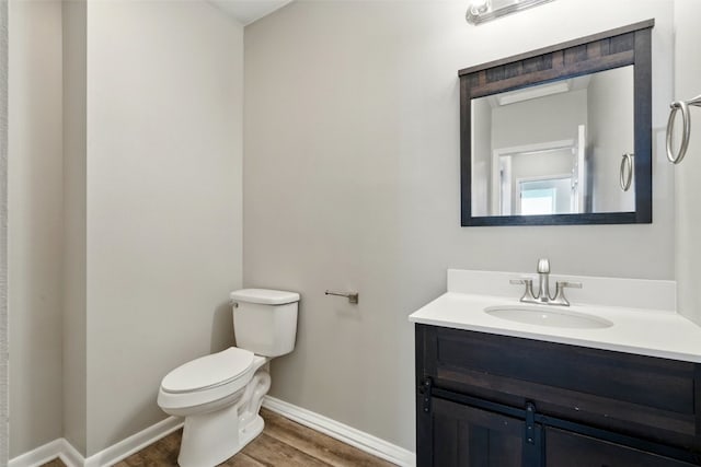 half bath with baseboards, toilet, wood finished floors, and vanity