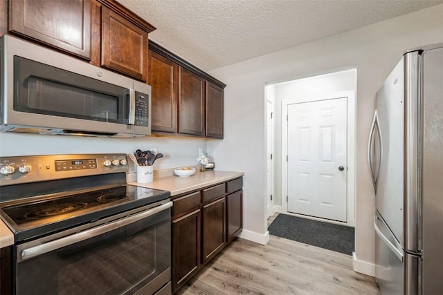 kitchen featuring stainless steel appliances, light wood finished floors, dark brown cabinetry, baseboards, and light countertops