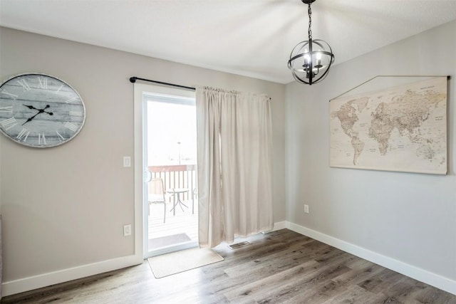 unfurnished dining area with a chandelier, wood finished floors, and baseboards
