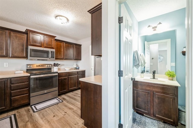 kitchen featuring stainless steel appliances, a sink, light countertops, a textured ceiling, and dark brown cabinets