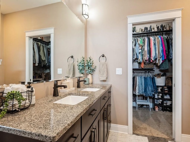 bathroom featuring a spacious closet, double vanity, and baseboards