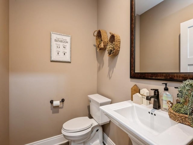 half bath featuring baseboards, toilet, and a sink