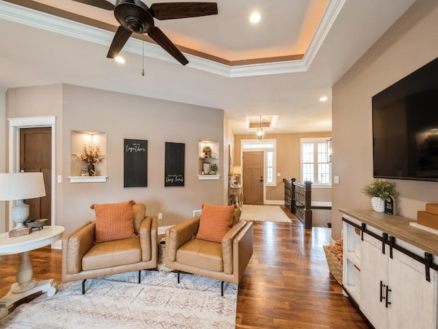 living area featuring crown molding, dark wood-type flooring, a ceiling fan, recessed lighting, and a raised ceiling