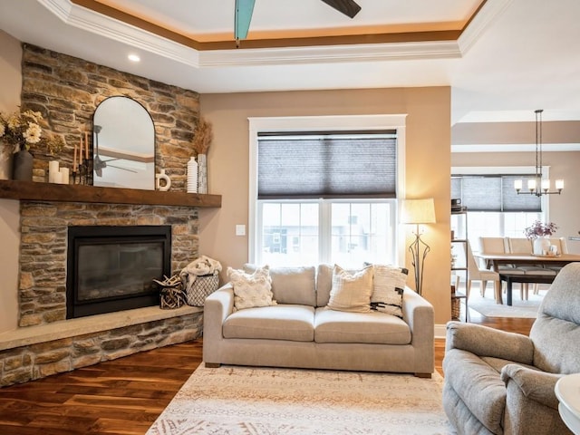 living area with a raised ceiling, ornamental molding, wood finished floors, plenty of natural light, and a chandelier