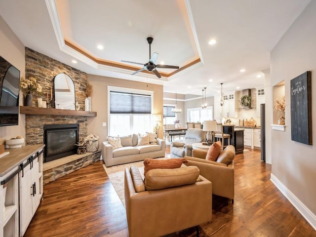 living room with a raised ceiling, ceiling fan, a fireplace, ornamental molding, and dark wood-type flooring