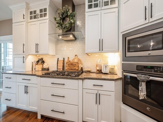 kitchen featuring gas cooktop, wall chimney range hood, dark stone countertops, white cabinets, and tasteful backsplash