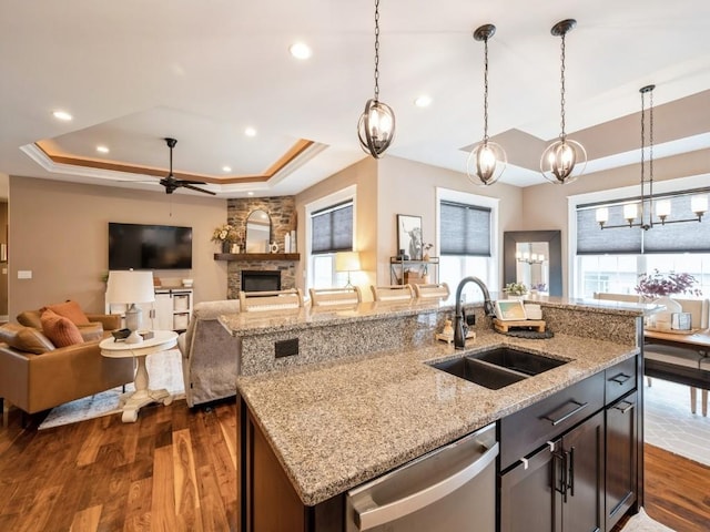 kitchen with dishwasher, a sink, a raised ceiling, ceiling fan, and dark wood-type flooring