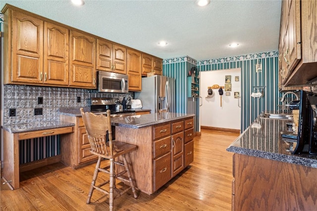 kitchen featuring stainless steel appliances, a sink, brown cabinets, light wood-type flooring, and a center island