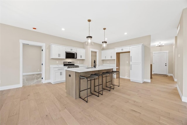 kitchen with stainless steel appliances, a sink, light wood-type flooring, white cabinetry, and an island with sink