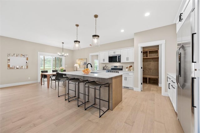 kitchen featuring stainless steel appliances, a sink, light wood finished floors, a kitchen bar, and baseboards