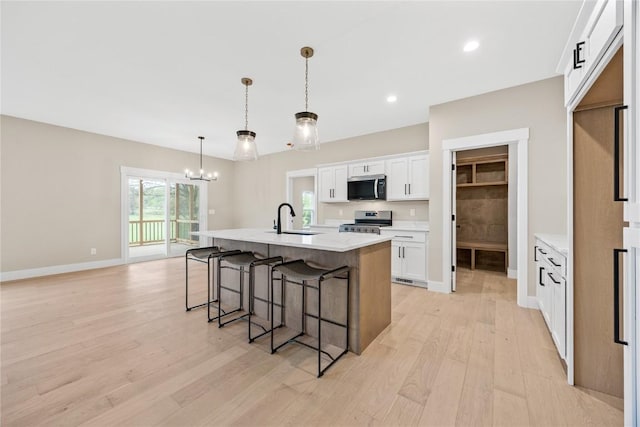 kitchen featuring appliances with stainless steel finishes, a sink, light wood-style flooring, a kitchen breakfast bar, and a chandelier