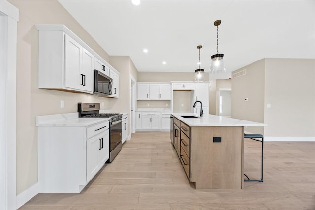 kitchen with appliances with stainless steel finishes, a sink, baseboards, light wood finished floors, and white cabinetry
