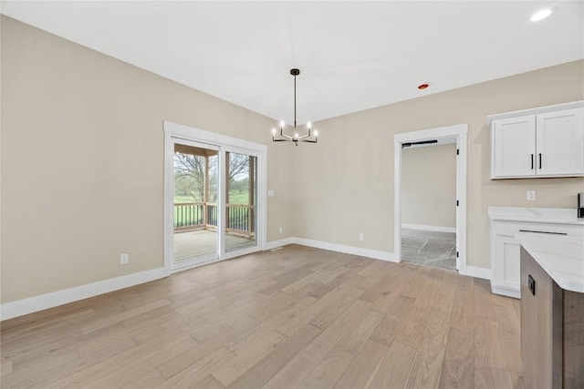 unfurnished dining area with a chandelier, light wood-style floors, and baseboards