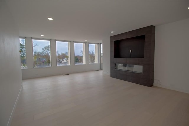 unfurnished living room with recessed lighting, a tiled fireplace, light wood-type flooring, and baseboards
