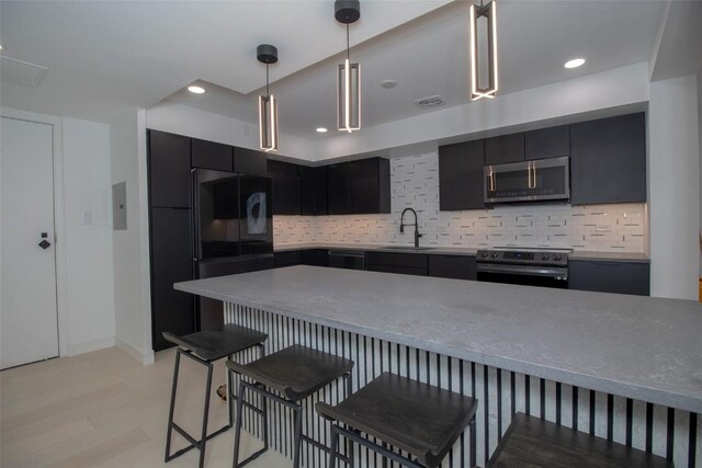 kitchen with appliances with stainless steel finishes, dark cabinetry, a breakfast bar, a sink, and hanging light fixtures