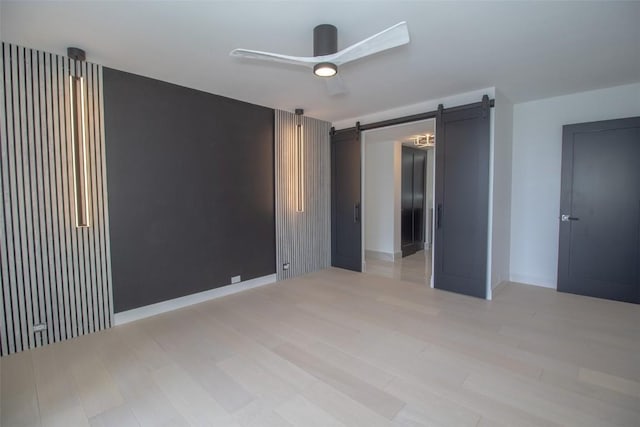 empty room featuring a barn door, light wood finished floors, and baseboards