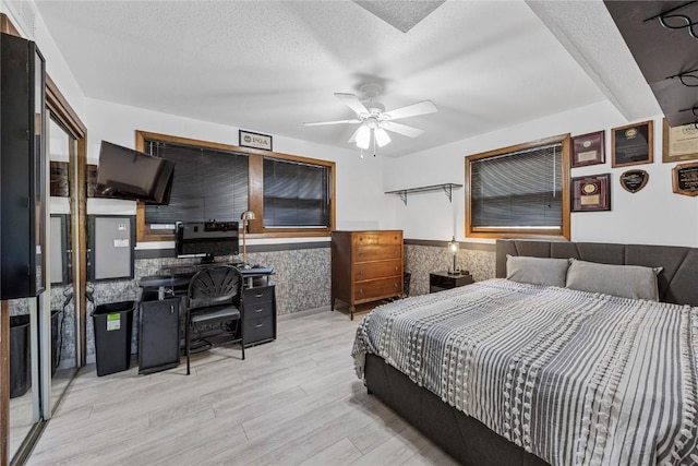 bedroom with a wainscoted wall, light wood-style floors, and a textured ceiling