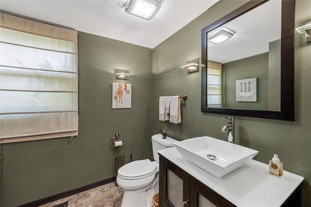 half bath with baseboards, toilet, a textured ceiling, and vanity