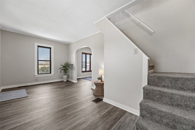 unfurnished living room featuring arched walkways, stairway, dark wood-style floors, and baseboards