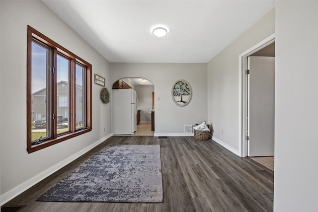 foyer with arched walkways, dark wood-type flooring, and baseboards