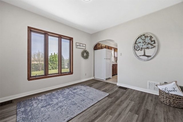 foyer featuring arched walkways, baseboards, and dark wood finished floors