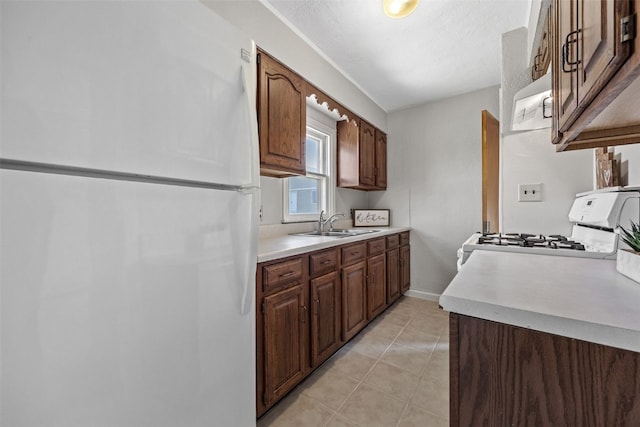 kitchen with white appliances, light countertops, light tile patterned floors, a sink, and baseboards
