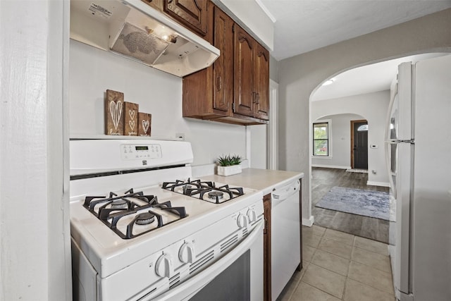 kitchen with white appliances, arched walkways, under cabinet range hood, light countertops, and light tile patterned flooring