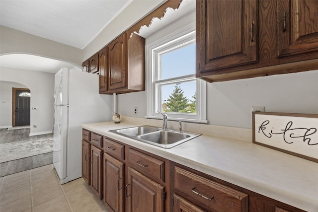 kitchen featuring a sink, arched walkways, light countertops, and freestanding refrigerator