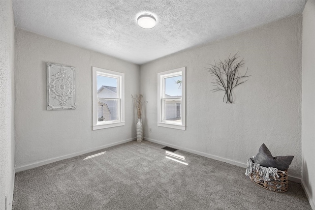 carpeted spare room featuring a textured ceiling and baseboards