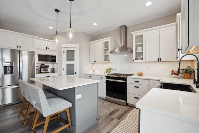 kitchen featuring stainless steel appliances, wall chimney range hood, a sink, a center island, and wood finished floors