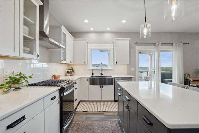 kitchen with a sink, wall chimney range hood, range with gas cooktop, white cabinetry, and light countertops