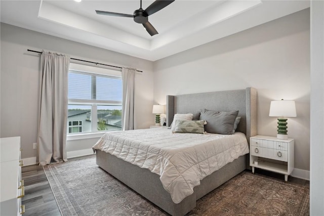 bedroom with a raised ceiling, dark wood finished floors, baseboards, and a ceiling fan
