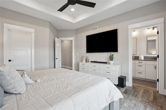 bedroom with wood finished floors, ceiling fan, connected bathroom, recessed lighting, and a raised ceiling