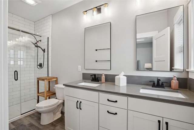 bathroom featuring toilet, wood finished floors, a stall shower, and double vanity