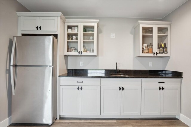 kitchen with freestanding refrigerator, a sink, white cabinetry, and dark stone counters