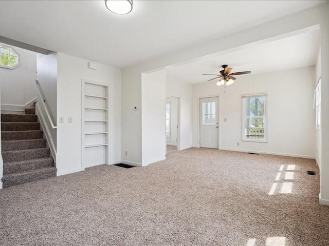 unfurnished living room featuring built in features, stairway, carpet, a ceiling fan, and baseboards