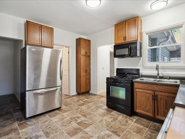 kitchen with black appliances, a sink, stone tile flooring, dark countertops, and brown cabinets