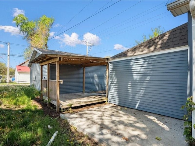 view of side of home with a patio, a wooden deck, and roof with shingles