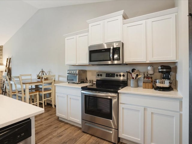 kitchen featuring appliances with stainless steel finishes, lofted ceiling, white cabinets, light wood-style flooring, and light countertops