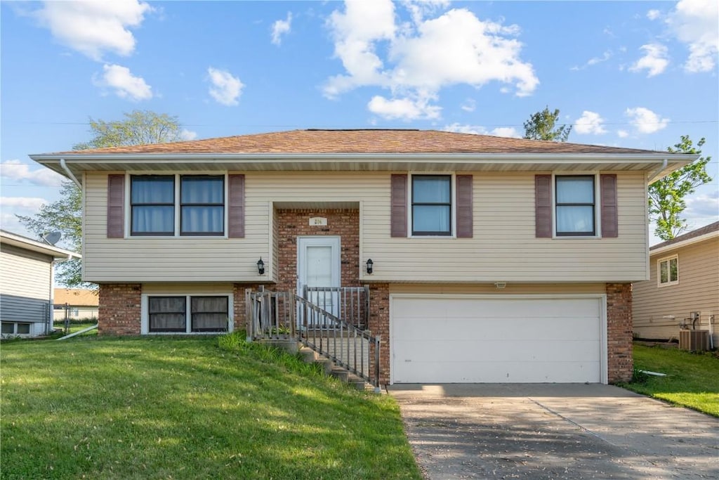 raised ranch featuring an attached garage, brick siding, central AC, concrete driveway, and a front yard
