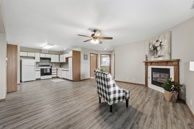 living area with wood finished floors, a tile fireplace, ceiling fan, and baseboards