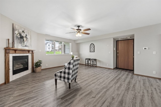 living room featuring wood finished floors, ceiling fan, a tile fireplace, and baseboards