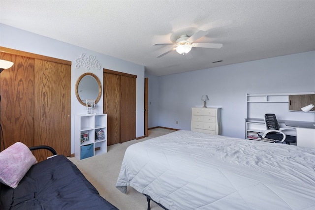 bedroom featuring light carpet, a textured ceiling, ceiling fan, and two closets