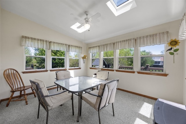 dining area with a skylight, baseboards, vaulted ceiling, light colored carpet, and a ceiling fan