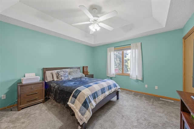 bedroom with a raised ceiling, carpet floors, baseboards, a textured ceiling, and ceiling fan
