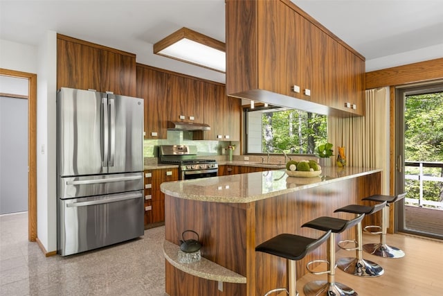 13 Woodland Hts, Iowa City, IA 52240 - kitchen featuring appliances with stainless steel finishes, under cabinet range hood, brown cabinetry, and a peninsula